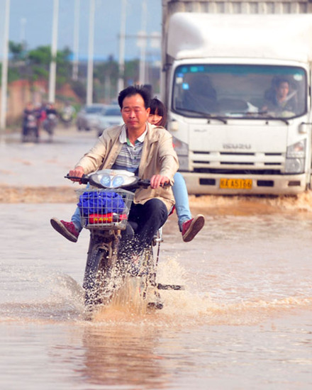 People wade through water on a bicycle in Nanning, capital of the Guangxi Zhuang autonomous region, on Tuesday. Several cities in the region have issued rainstorm alerts. HUANG XIAOBANG / XINHUA
