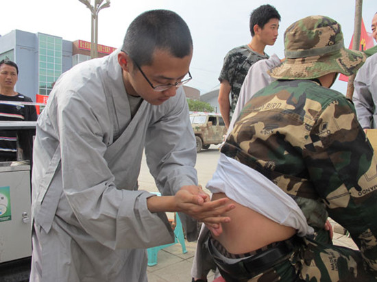 Shi Yanyun, a rescue team member from Shaolin Temple, treats a volunteer who hurt his back during earthquake rescue operations in Lushan, Sichuan province, on Thursday. AN BAIJIE / CHINA DAILY