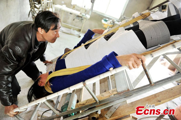 Zhu Qinghua manipulates the stone removing bed to keep his wife in an upside-down position. (Photo/CFP) Zhu Qinghua manipulates the stone removing bed to keep his wife in an upside-down position. (Photo/CFP)