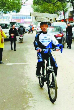 Zhang Xunmu rides a bicycle with a 34 kg millstone and a 15 kg stone block on his head. (Photo/Wuhan Evening News) Zhang Xunmu rides a bicycle with a 34 kg millstone and a 15 kg stone block on his head. (Photo/Wuhan Evening News)