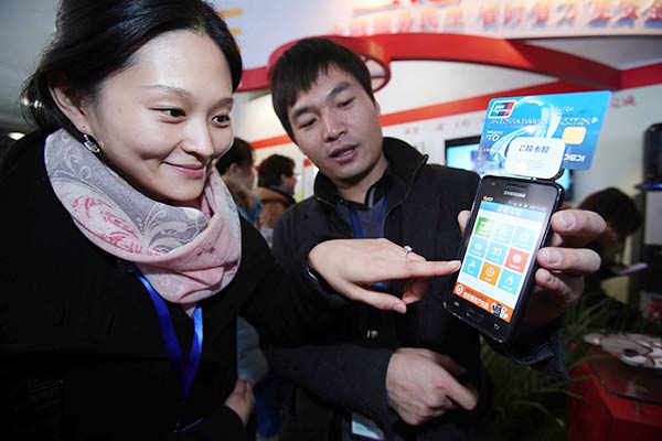 An employee shows a visitor how to use online payment functions on mobile devices at an expo in Beijing.(Photo/China Daily) An employee shows a visitor how to use online payment functions on mobile devices at an expo in Beijing.(Photo/China Daily)