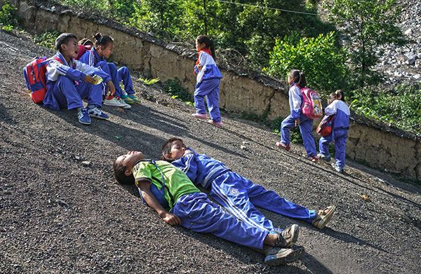 Children from Atuler village in Sichuan province take a rest during their regular long trudge to school. CHEN JIE/ FOR CHINA DAILY Children from Atuler village in Sichuan province take a rest during their regular long trudge to school. CHEN JIE/ FOR CHINA DAILY