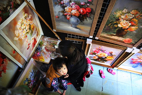 An oil painter works on a still life painting as her daughter sits on her lap at an art gallery in Dafen village, Shenzhen, Guangdong province. (Photo by Xu Yuanchang/China Daily) An oil painter works on a still life painting as her daughter sits on her lap at an art gallery in Dafen village, Shenzhen, Guangdong province. (Photo by Xu Yuanchang/China Daily)