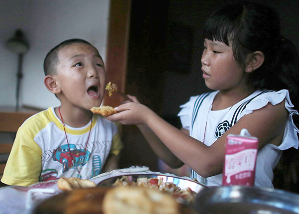 Guo's sister helps him eat supper while their parents are away from home. (Photo/China Daily) Guo's sister helps him eat supper while their parents are away from home. (Photo/China Daily)
