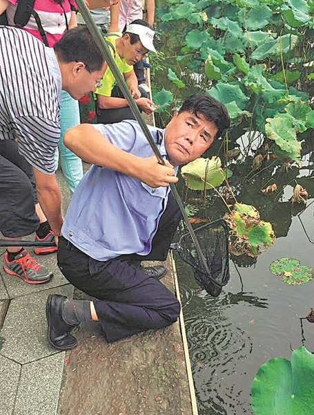 Hangzhou police officer Zhou Xiangjun helps a visitor in August to retrieve an item that had fallen into West Lake. (Photo provided to CHINA DAILY) Hangzhou police officer Zhou Xiangjun helps a visitor in August to retrieve an item that had fallen into West Lake. (Photo provided to CHINA DAILY)