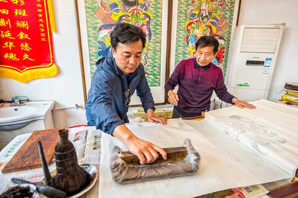 Huo Qingshun, an inheritor of the Yangliuqing New Year painting, teaches a visitor to use an ink mold to create a sketch of the traditional painting, April 28, 2017. (Photo by Liu Jie/provided to chinadaily.com.cn) Huo Qingshun, an inheritor of the Yangliuqing New Year painting, teaches a visitor to use an ink mold to create a sketch of the traditional painting, April 28, 2017. (Photo by Liu Jie/provided to chinadaily.com.cn)