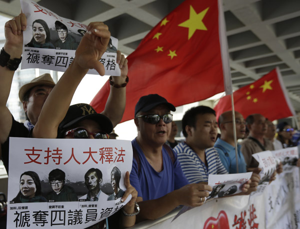 Residents outside the high court hold placards and shout slogans on Friday to support the disqualification of four lawmakers who did not follow the requirements when they took their oaths to serve on the Legislative Council in October last year. (Photo by ROY LIU/CHINA DAILY) Residents outside the high court hold placards and shout slogans on Friday to support the disqualification of four lawmakers who did not follow the requirements when they took their oaths to serve on the Legislative Council in October last year. (Photo by ROY LIU/CHINA DAILY)