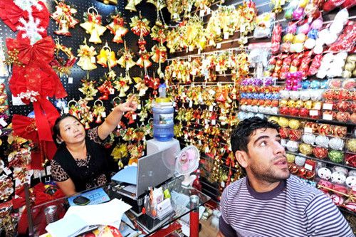 A stall owner shows to an international trader Christmas decorations in Yiwu. Business men in the manufacturing center see orders for Christmas season from North America bounce back. [Photo/Xinhua]