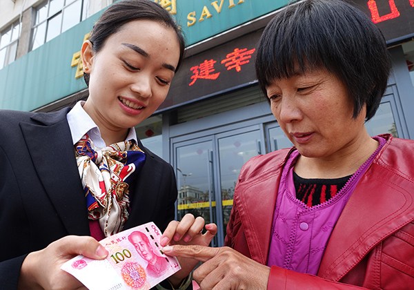 An employee shows a customer anti-counterfeiting marks on a new banknote at Postal Savings Bank of China's branch in Zaozhuang, Shandong province. (Photo/China Daily) An employee shows a customer anti-counterfeiting marks on a new banknote at Postal Savings Bank of China's branch in Zaozhuang, Shandong province. (Photo/China Daily)
