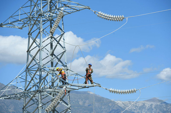 An employee connects electrical cables atop a 30-meter-high, 110 kV power transmission tower in the Tibet autonomous region. State Grid Corp of China, the country's largest grid operator, will further push for a unified national electricity market. (Photo by Song Weixing/For China Daily)
