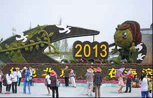 Visitors pose with the mascot of the garden expo before a flower bed. 