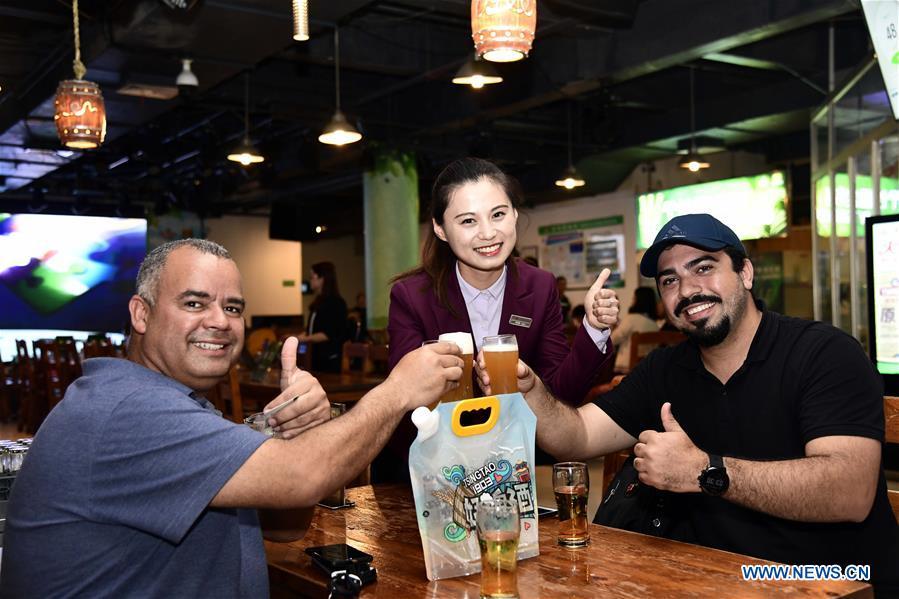 Tourists toast with Tsingtao Beer in Qingdao, a coastal city in east China\'s Shandong Province, May 17, 2018. Home to Tsingtao Beer and home appliance giant Haier, Qingdao is becoming a more attractive place to run important multilateral events. In June, the coastal city will host the 18th summit of the Shanghai Cooperation Organization (SCO). (Xinhua/Guo Xulei)