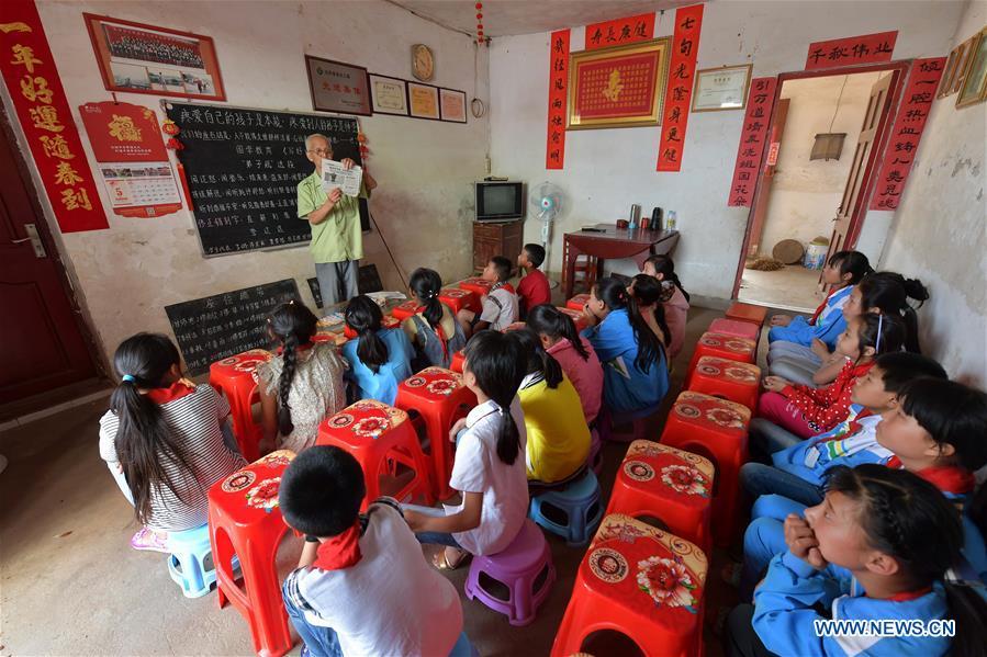 Miao Yanxiang reads a report of good deeds for children at the caring station for left-behind children at his home in Shibu Town, Nanchang City of east China\'s Jiangxi Province, May 23, 2018. Miao, over 70, established a caring station for left-behind children at his own house in 2009, where he provided free place for children to do homework and study after school. Having received more than 3,000 children over the past nine years, Miao is satisfied with his voluntary work as he see the progress of the children. (Xinhua/Peng Zhaozhi)