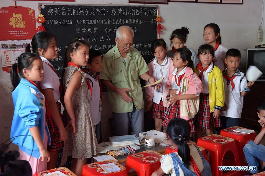 Miao Yanxiang awards children doing well on homework with prizes he bought at the caring station for left-behind children at his home in Shibu Town, Nanchang City of east China\'s Jiangxi Province, May 23, 2018. Miao, over 70, established a caring station for left-behind children at his own house in 2009, where he provided free place for children to do homework and study after school. Having received more than 3,000 children over the past nine years, Miao is satisfied with his voluntary work as he see the progress of the children. (Xinhua/Peng Zhaozhi)