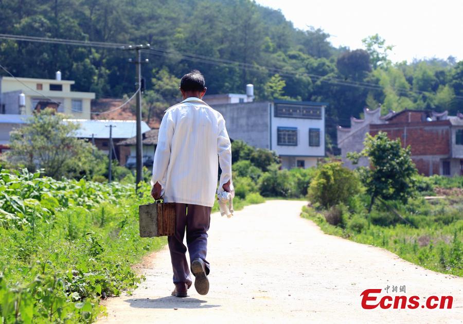 Barber Hu Daofa walks in a village in Zhuangbu Countryside, Huichang County, East China’s Jiangxi Province. Hu, 73, started travelling around nearby villages offering door-to-door haircutting, shaving, and ear-cleaning in 1966, charging an annual fee of 130 yuan for three visits a month. Hu can’t ride a bicycle, so he walks. Most of his customers are children and elderly people. (Photo: China News Service/Jiang Tao)