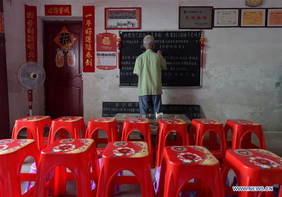 Miao Yanxiang writes old sayings on the blackboard of the caring station for left-behind children at his home in Shibu Town, Nanchang City of east China\'s Jiangxi Province, May 23, 2018. Miao, over 70, established a caring station for left-behind children at his own house in 2009, where he provided free place for children to do homework and study after school. Having received more than 3,000 children over the past nine years, Miao is satisfied with his voluntary work as he see the progress of the children. (Xinhua/Peng Zhaozhi)