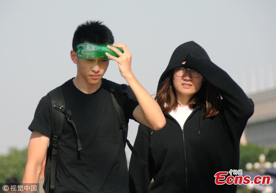 Tourists try all possible ways, including wearing hats, to shade themselves from the sun near the Forbidden City and Tiananmen Square in Beijing, March 31, 208, as temperatures rose to a record 35 degrees centigrade. Beijing issued a yellow alert against high temperatures on Thursday. (Photo/VCG)