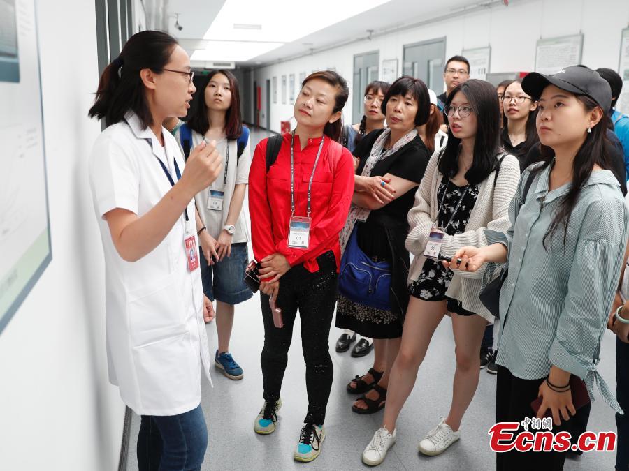 A volunteer talks to visitors about cultural relics restoration at a \'hospital\' in the Palace Museum in Beijing, June 9, 2018. As part of ongoing activities held for China\'s Cultural and Natural Heritage Day, the first batch of 40 people watched \'doctors\' repairing pieces from some of the museum\'s collections, including pieces of calligraphy, paintings, bronzeware and clocks, under the guidance of volunteers. Established in December 2016, the restoration hospital is located in the west of the Palace Museum. The facility covers 13,000 square meters and has the nation\'s most-advanced restoration studios. (Photo: China News Service/Liu Guanguan)