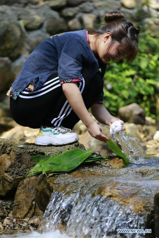 A woman cleans leaves for making Zongzi, a pyramid-shaped dumpling made of glutinous rice wrapped in bamboo or reed leaves, to greet the upcoming Dragon Boat Festival in a rivulet of Zhangjiajie City, central China\'s Hunan Province, June 11, 2018. (Xinhua/Wu Yongbing)