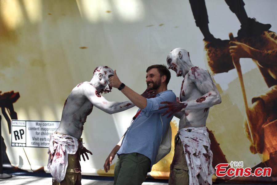 An attendee poses for a picture with zombies at E3, the world\'s largest video game industry convention in Los Angeles, California, U.S., June 13, 2018. (Photo: China News Service/Zhang Shuo)
