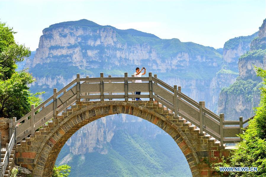 A tourist takes photos in Shenlongwan scenic area in Changzhi City, north China\'s Shanxi Province, June 13, 2018. A 1,526-meter-long road was built along the cliffs to connect isolated Shenlongwan to the outside. The construction of this miraculous road lasted for fifteen years from 1985 to 2000, and was built purely by villagers of Shenlongwan. Thanks to this road, villagers here now cast off poverty by developing tourism. (Xinhua/Cao Yang)