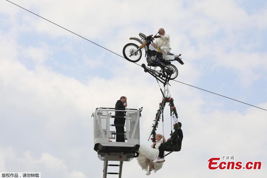 Pastor Stefan Gierung, left, stands in a cage atop of a fire service ladder in front of bride Nicole Backhaus, center, and groom Jens Knorr, right, both sitting in a swing dangling under a motorcycle with artist Falko Traber, top, during the wedding ceremony atop a tightrope in Stassfurt, Germany, June 16, 2018. (Photo/Agencies)
