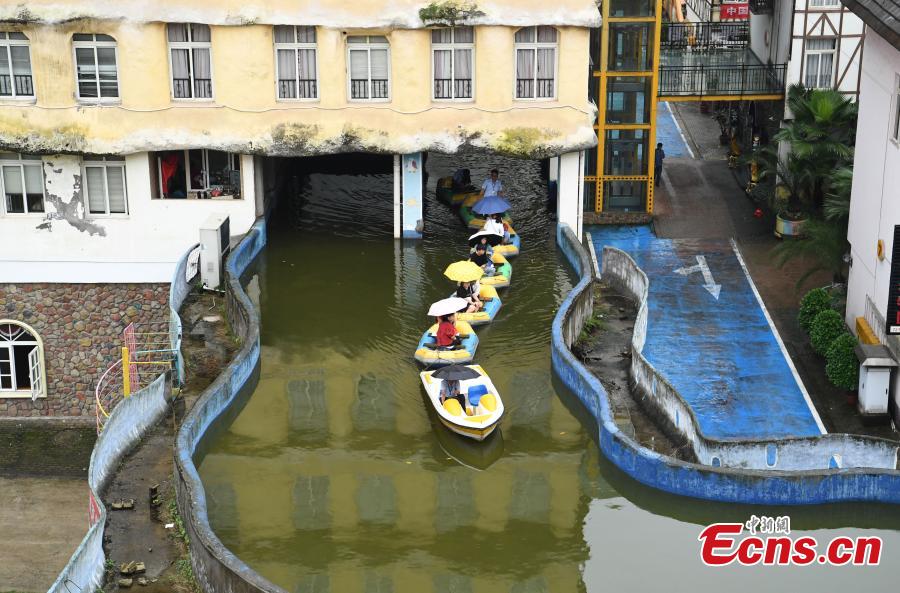 Tourists take boats on an artificial canal during their visit to a wine town in Fuling District, Southwest China’s Chongqing Municipality, June 20, 2018. The five-kilometer-long canal includes a section that passes through a building. (Photo: China News Service/Chen Chao)