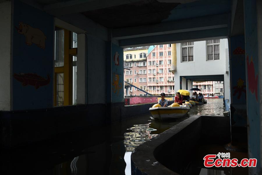Tourists take boats on an artificial canal during their visit to a wine town in Fuling District, Southwest China’s Chongqing Municipality, June 20, 2018. The five-kilometer-long canal includes a section that passes through a building. (Photo: China News Service/Chen Chao)
