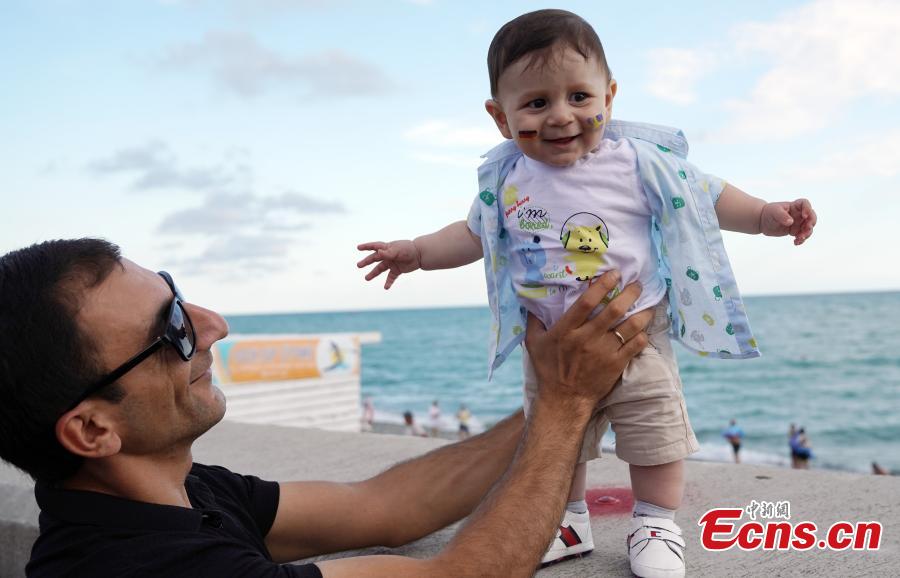 A man carries a child with German and Swedish flags painted on his face before a World Cup match on the Black Sea coast in Russia, June 24, 2018. (Photo: China News Service/Mao Jianjun)