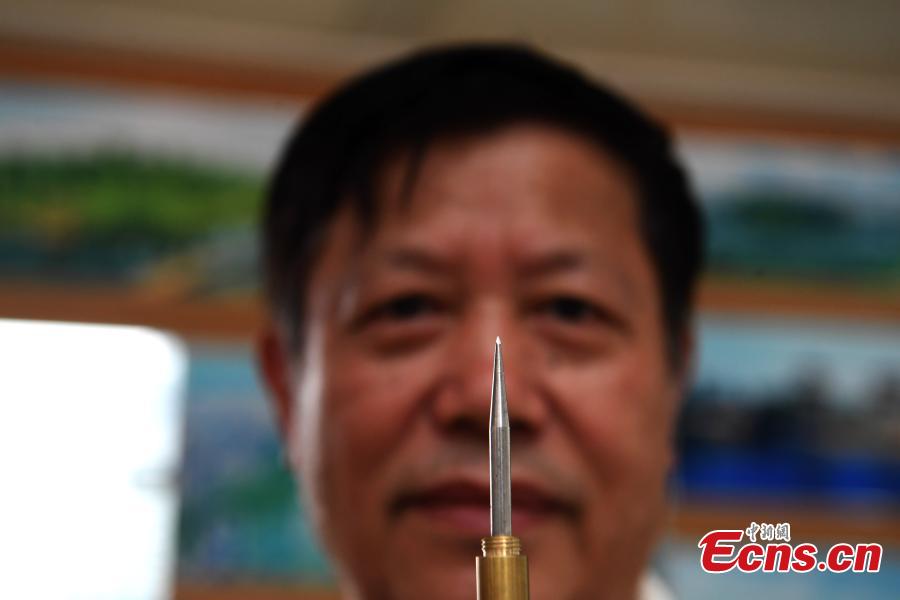 Pan Qihui shows a tool he uses to make miniature carvings at an exhibition in Chongqing, June 23, 2018. The smallest characters carved by Pan are as thin as a hair and a magnifying glass is needed to see them. (Photo: China News Service/Chen Chao)
