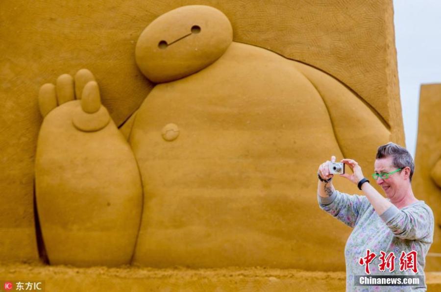 A visitor takes photos beside a sculpture during the Sand Sculpture Festival \