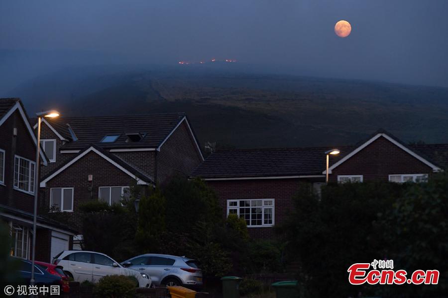The full moon rises behind burning moorland as a large wildfire sweeps across the moors between Dovestones and Buckton Vale in Stalybridge, Greater Manchester in Stalybridge, England, June 26, 2018.  (Photo/VCG)