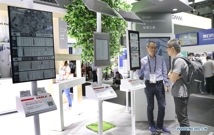 A staff member (L) introduces solar-powered bus stop display panels based on electronic ink and wireless network technologies during the Mobile World Conference Shanghai (MWCS) 2018 in east China\'s Shanghai, June 27, 2018. The three-day MWCS 2018 kicked off at the Shanghai New International Expo Center on Wednesday, showing trending mobile products, services and technologies. (Xinhua/Fang Zhe)