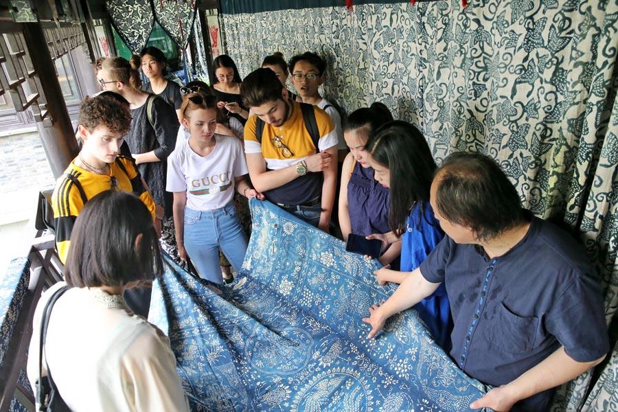 Chinese and British students from the China Academy of Art\'s creative fashion design camp listen to explanations of patterns on traditional Chinese blue calico in Nantong, East China\'s Jiangsu Province, on July 3, 2018. This year\'s camp features students from eight British universities including Southampton\'s Solent University and Edinburgh University, as well as others from Shanghai Institute of Design of the China Academy of Art. (Photo/Asianewsphoto)