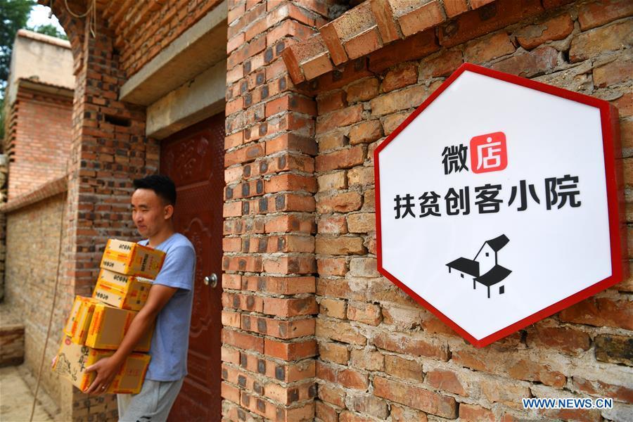 A deliveryman carries packages at a delivery post in Lingtou Village of Wuxiang County, north China\'s Shanxi Province, July 3, 2018. Online business helped villagers sell their farm products, significantly increasing the average incomes of local residents in Lingtou Village. (Xinhua/Zhan Yan)
