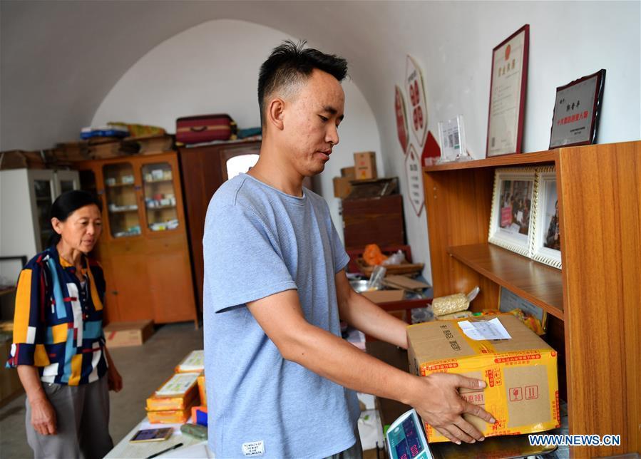 A deliveryman weighs the package at a delivery post in Lingtou Village of Wuxiang County, north China\'s Shanxi Province, July 3, 2018. Online business helped villagers sell their farm products, significantly increasing the average incomes of local residents in Lingtou Village. (Xinhua/Zhan Yan)