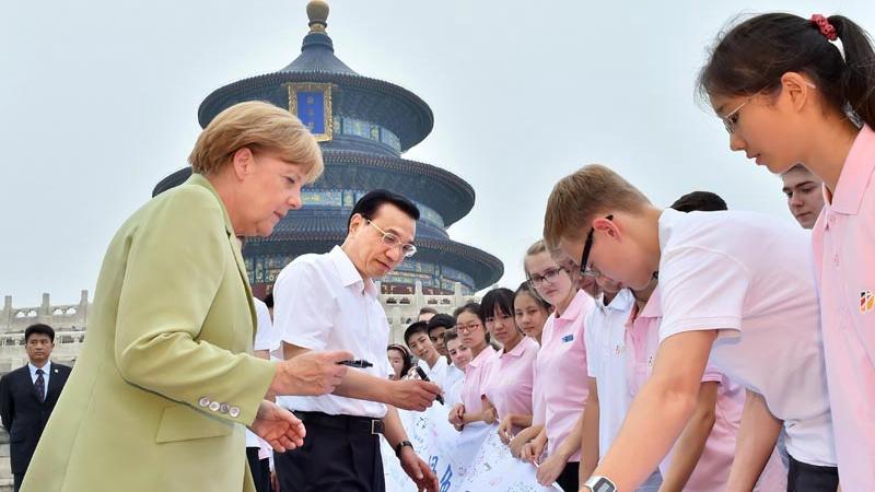 Premier Li and Chancellor Merkel sign on a memorial banner when meeting with youngsters attending the closing ceremony of the \