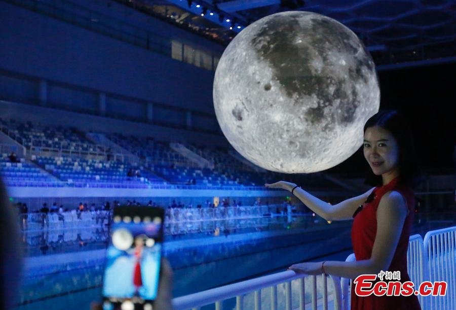 Visitors take photos of a huge moon model during an exhibition on moon held at the National Aquatic Center or \