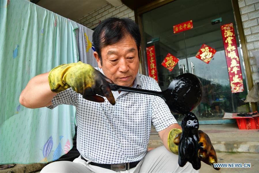 Local handicraftsman Ren Guohe colours a clay statuette in Jinzhuang Village of Huaiyang County, central China\'s Henan Province, July 9, 2018. Originated from ancient sacrificial ceremonies, the hand-made clay statuette \