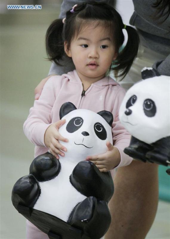 A girl plays with a papier-mache panda during an exhibition of the papier-mache artwork \