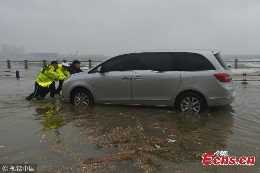 Police officers help move a car stranded in waves on a beach ahead of tropical storm Ampil in Qingdao City, East China’s Shandong Province, July 23, 2018. (Photo/VCG)