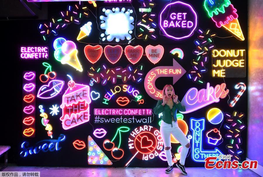 A visitor to Sugar Republic poses in front of a giant wall of neon signs in Melbourne on July 24, 2018. Sugar Republic is an interactive pop-up museum dedicated to the celebration of desserts, candy and all things sweet through 12 amazing sensory rooms.(Photo/Agencies)