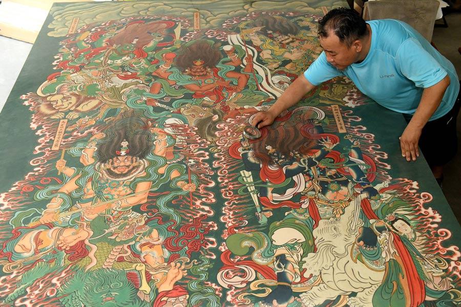 Yao Shulong checks his replica paintings of murals in Pilu Temple in his studio on July 24, 2018. (Photo/Xinhua)