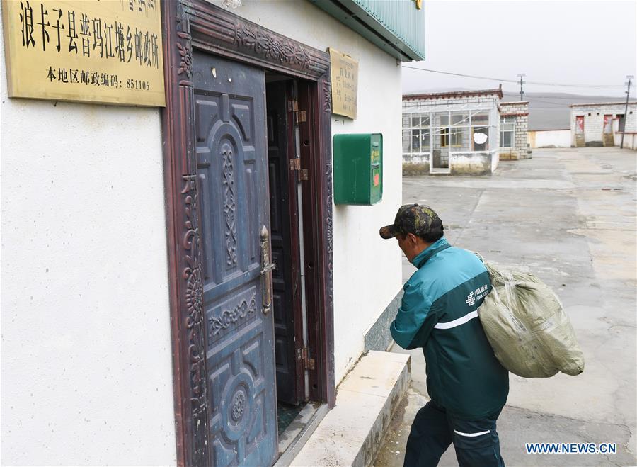 Postal courier Cering Quba carries a bag of mails to the township branch of China Post in Pumaqangtang Township of Nagarze County in Shannan, southwest China\'s Tibet Autonomous Region, July 23, 2018. In Pumaqantang Township, the highest township in China, working as a postal service staff means delivering mails to addresses at altitudes of 5,000 meters and above. Gesang Cering, 29, is a motorbike courier with the local township branch of China Post. Twice a week, Gesang calls on the plateau villages under the township on a 160-km route, coping with extreme oxygen and temperature conditions. Despite its harsh geography, Tibet Autonomous Region has substantially improved the local postal service over the four decades since China\'s reform and opening up. By the end of 2017, the postal road network had managed to cover all towns and counties within the autonomous region. (Xinhua/Li He)