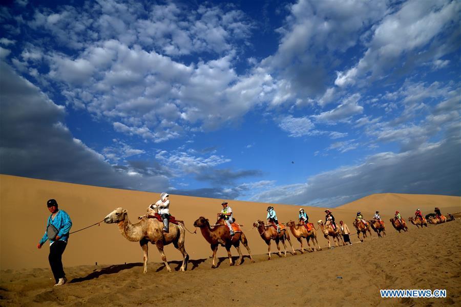 Tourists ride camels at the Mingsha Mountain and Crescent Spring scenic spot in Dunhuang, northwest China\'s Gansu Province, July 29, 2018. (Xinhua/Zhang Xiaoliang)