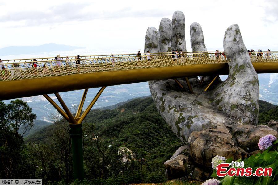 In this photograph taken on July 31, 2018, visitors walk along the 150-meter long Cau Vang \'Golden Bridge\' in the Ba Na Hills near Danang. Nestled in the forested hills of central Vietnam two giant concrete hands emerge from the trees, holding up a glimmering golden bridge crowded with gleeful visitors taking selfies at the country\'s latest eccentric tourist draw. Suspended 1400 meters above sea level, the bridge combines eight sections and stretches 150 meters long. (Photo/VCG)