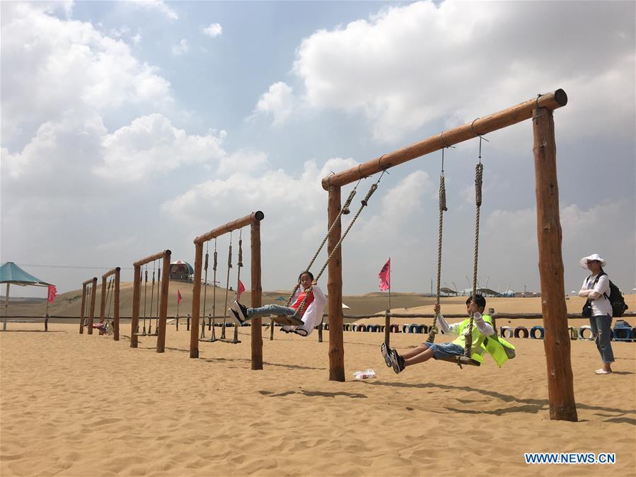 Tourists have fun at a scenic spot at the Kubuqi Desert in Erdos, north China\'s Inner Mongolia Autonomous Region, July 31, 2018. Kubuqi, the seventh largest desert in China, is a good example of China\'s success in alleviating desertification. About 6,460 square kilometers of the Kubuqi desert has been reclaimed in the last 30 years. (Xinhua/Zhang Shanchen)