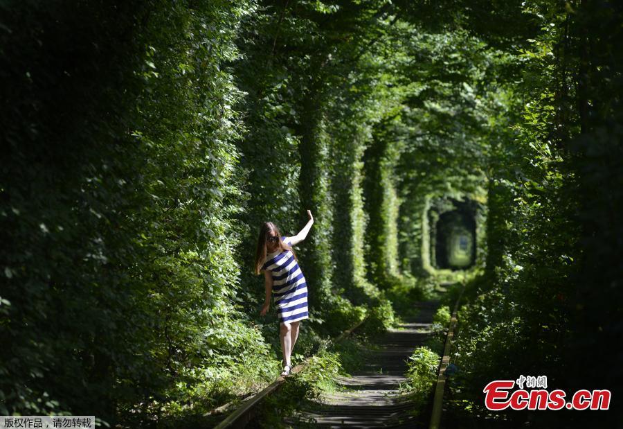 A girl walks along former railway tracks in the so-called \'Tunnel of Love\', surrounded by arches of intertwined trees, near the Ukrainian village of Klevan, Rivno region, Aug. 6, 2018. The tunnel of about five kilometers in length is a botanical phenomenon, which became a cult place for tourists and couples in love. The tourist legend says that wishes of couples in love will come true, if the couple passes through the tunnel. (Photo/Agencies)