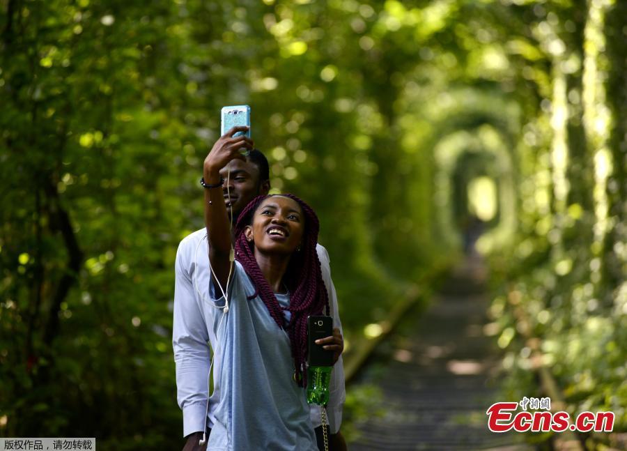 A couple takes selfies as they walk along former railway tracks surrounded by arches of intertwined trees in the so-called \'Tunnel of Love\', near the Ukrainian village of Klevan, Rivno region, Aug. 6, 2018. The tunnel of about five kilometers in length is a botanical phenomenon, which became a cult place for tourists and couples in love. The tourist legend says that wishes of couples in love will come true, if the couple passes through the tunnel. (Photo/Agencies)