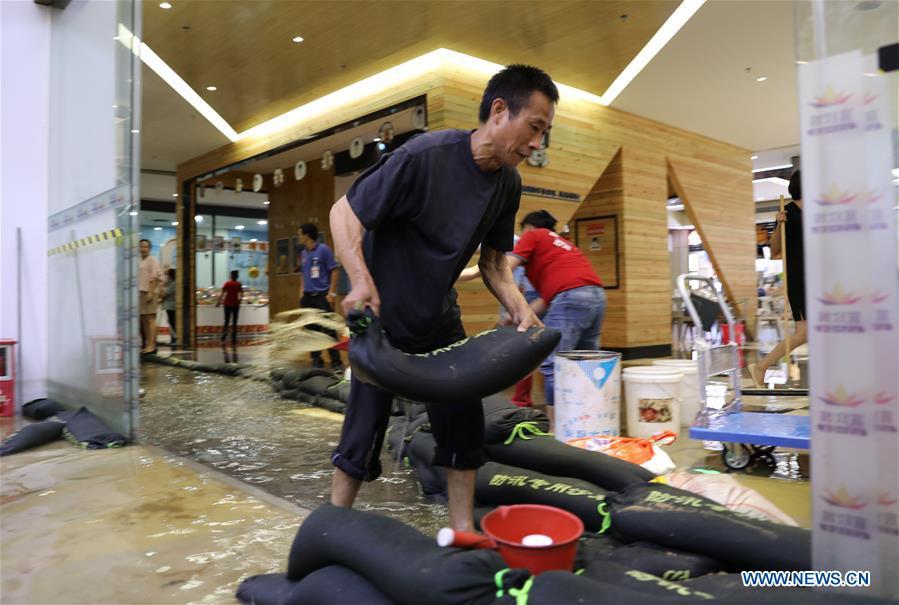 A staff of a shop carries a sand bag to keep away flood water in Haikou, south China\'s Hainan Province, Aug. 10, 2018. Hainan was hit by heavy rainfalls under the influence of a tropical depression on Friday, which triggered a red alert for rainstorms in seven cities and counties, including Haikou. (Xinhua/Wang Junfeng)